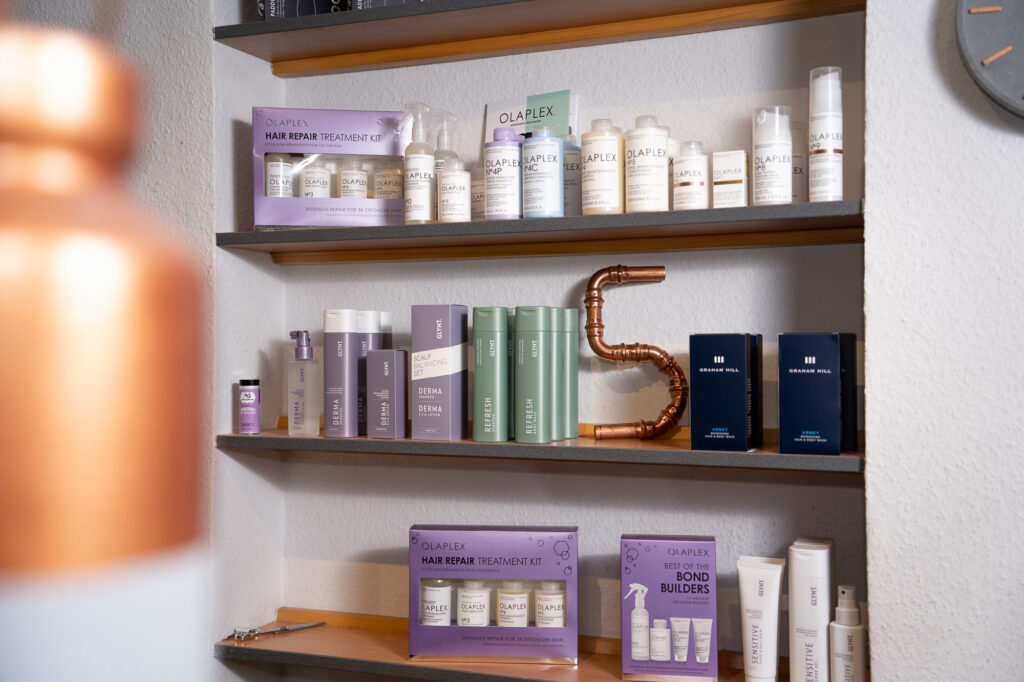 Shampoos und Pflegeprodukte fuer die Haare stehen in einem Regal eines Friseursalons