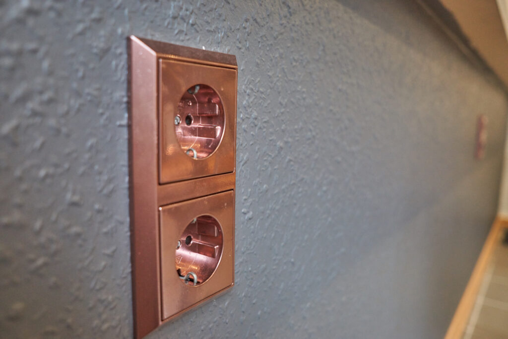 seitliche Sicht auf kupferne Doppelsteckdose auf dunkelgrauer Wand