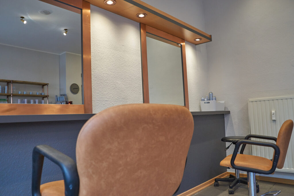 zwei Stuehle in einem Friseursalon vor einem großen Spiegel