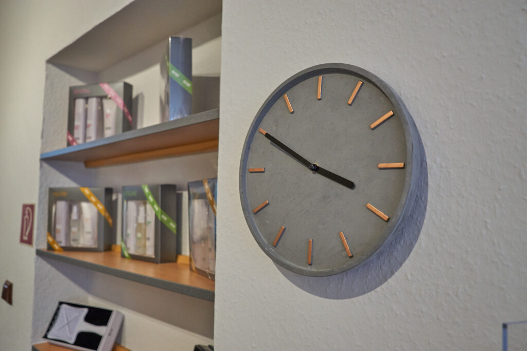 runde Uhr mit schwarzen Zeigern haengt an Wand neben Regal
