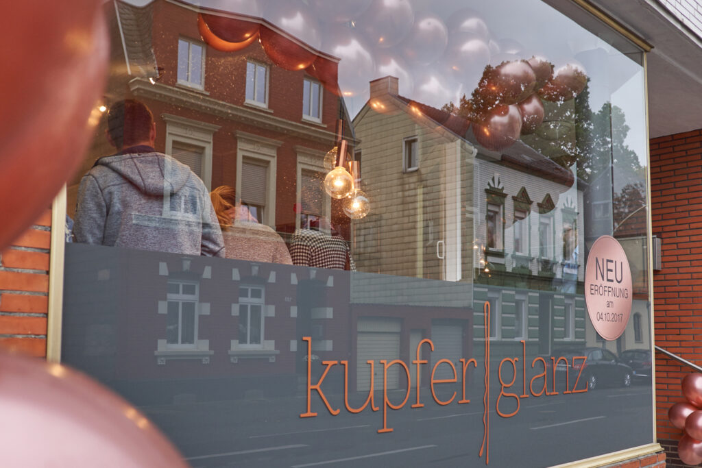 Sicht auf Schaufenster mit Schriftzug von Friseursalon Kupferglanz in Moenchengladbach, Menschen im Hintergrund