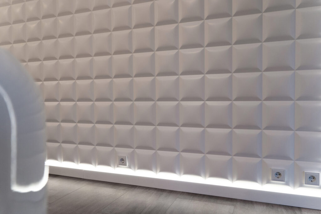 weiße gewoelbte Kacheln an der Wand mit LEDs an der Fußleiste mit drei Steckdosen