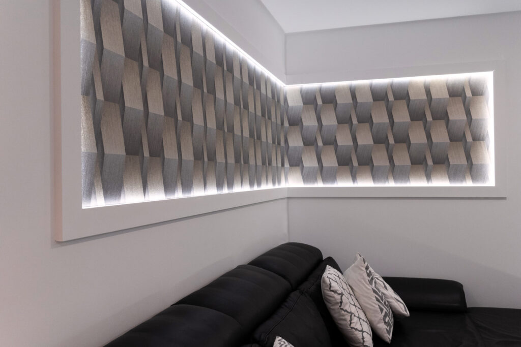 Abstrakte Formkunst mit LEDs haengt im 90°-Winkel über einem Sofa auf weißer Wand