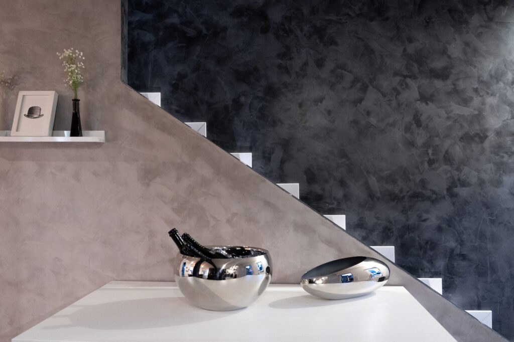 Zwei silberne Schuesseln stehen auf weißer Kommode, daneben hängt ein kleines Regal mit Dekoration